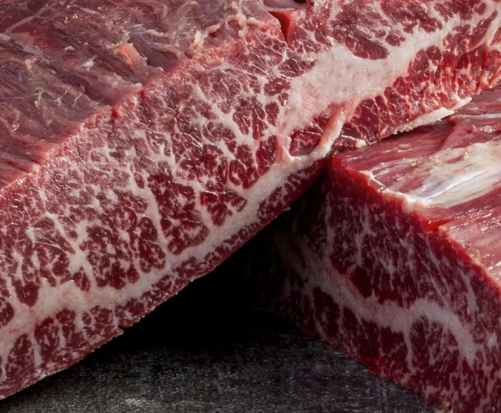 Nahaufnahme von zwei Stücken rohem, tiefrotem Rindfleisch mit sehr ausgeprägter, feiner weißer Marmorierung, die auf hohe Qualität hindeutet.