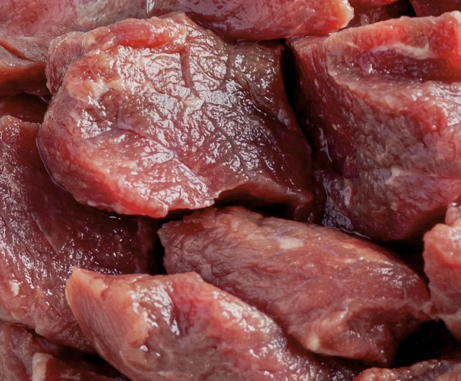 Nahaufnahme von vielen rohen, gewürfelten Fleischstücken, die dicht beieinander liegen. Das Fleisch ist rot und glänzend, mit sichtbaren Fasern und etwas Fett.