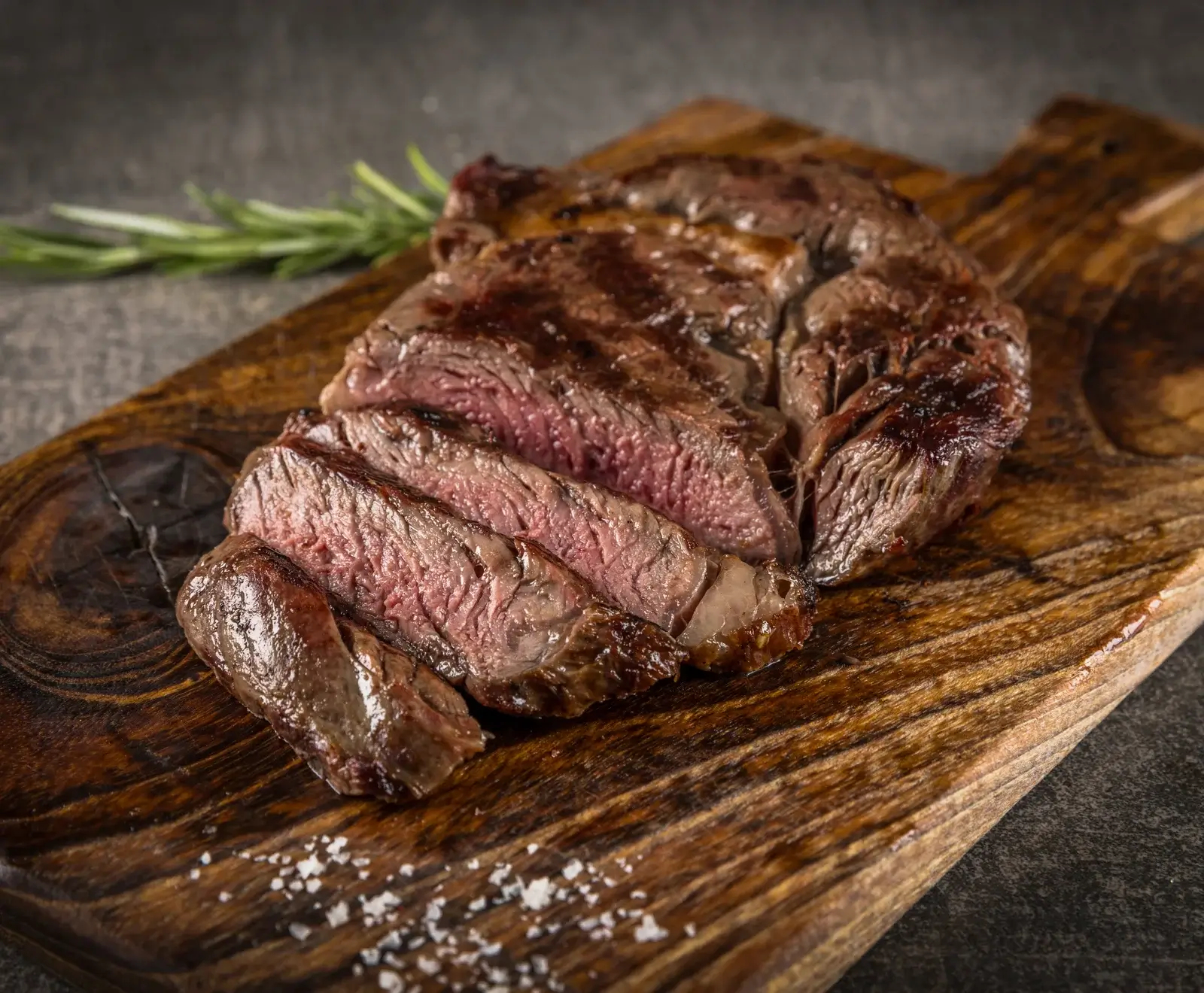 Ein medium-rare gegartes, in Scheiben geschnittenes Steak auf einem rustikalen Holzbrett, garniert mit Rosmarin und Meersalz.
