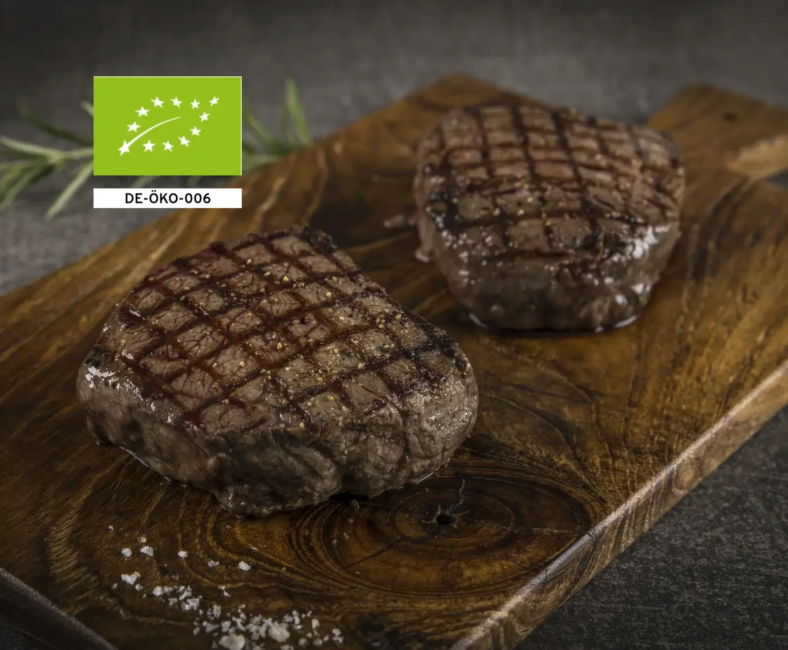 Zwei gegrillte Bio-Rindersteaks auf einem Holzbrett, mit EU-Bio-Logo und Kennung