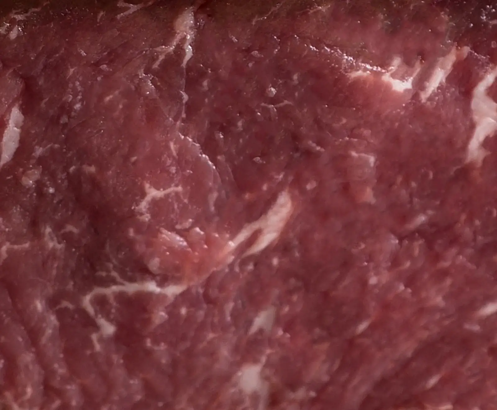Nahaufnahme von rotem, rohem Fleisch mit sichtbarer weißer Fettmarmorierung und faseriger Textur.