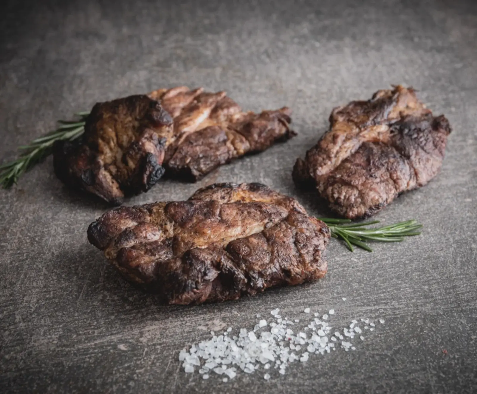 Gegrillte Steaks mit Rosmarin auf einem dunklen Hintergrund mit Salzkristallen.